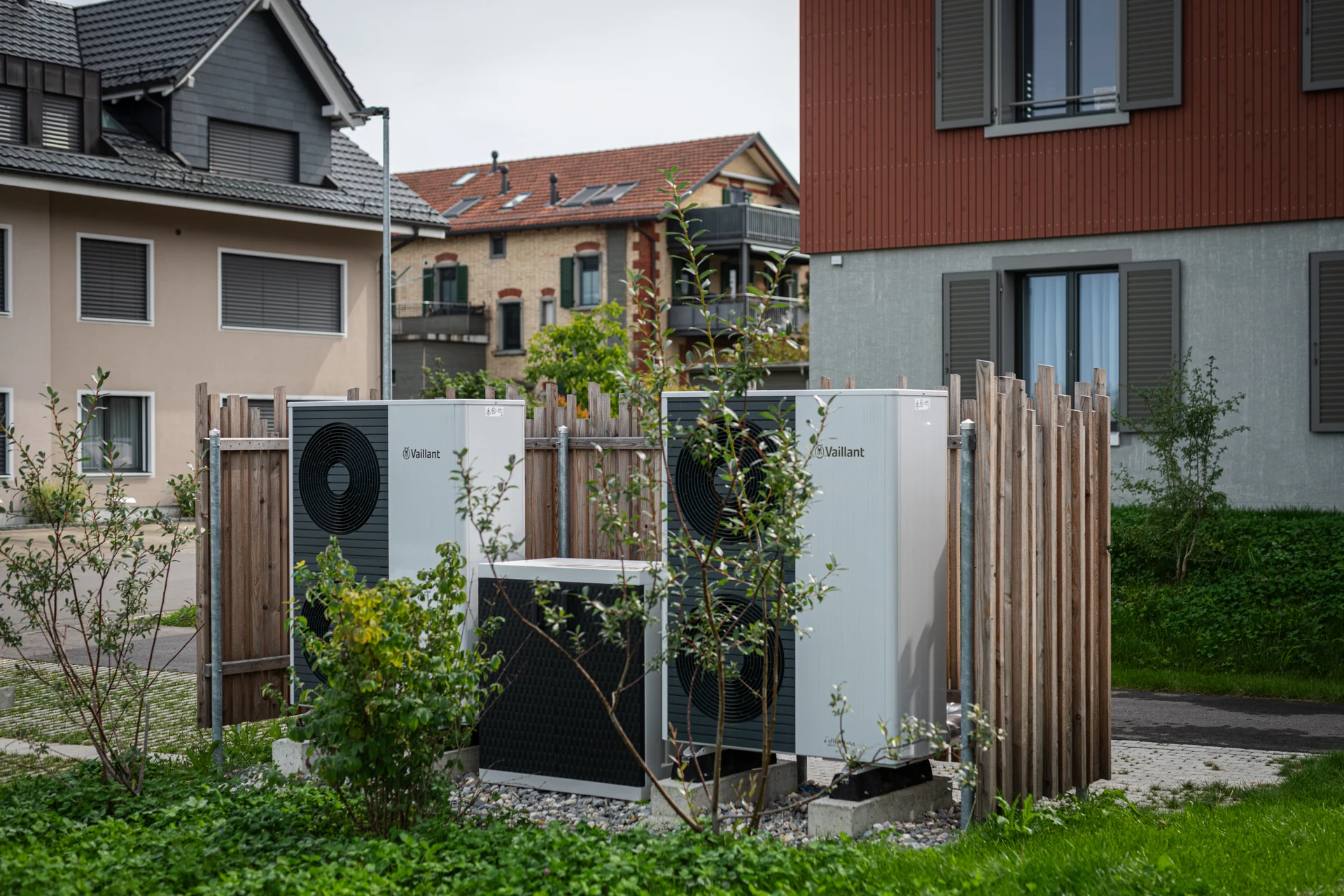 Zwei Wärmepumpen-Ausseneinheiten im Garten vor Wohnhäusern