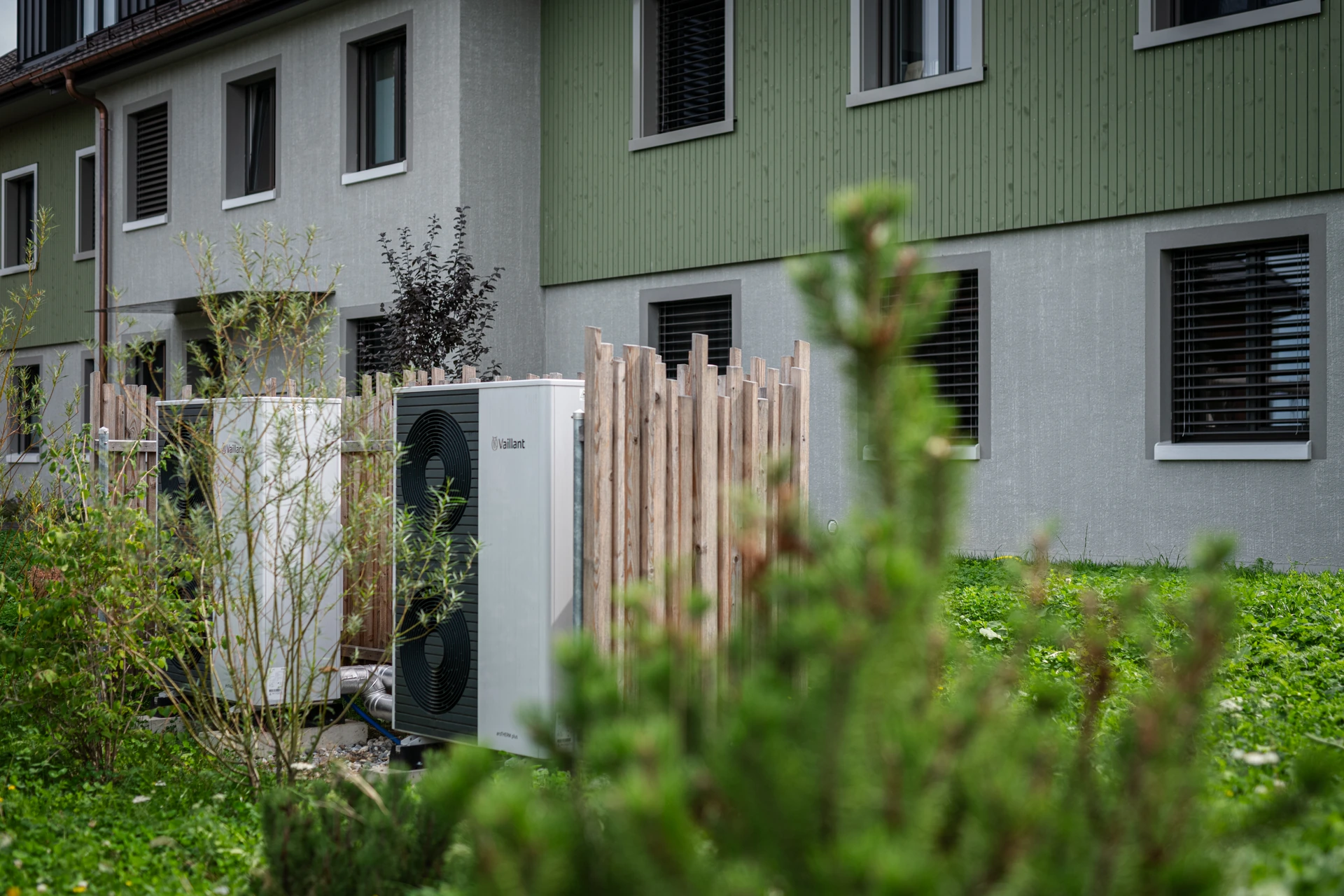 Wärmepumpe neben einer bepflanzten Grundstücksgrenze