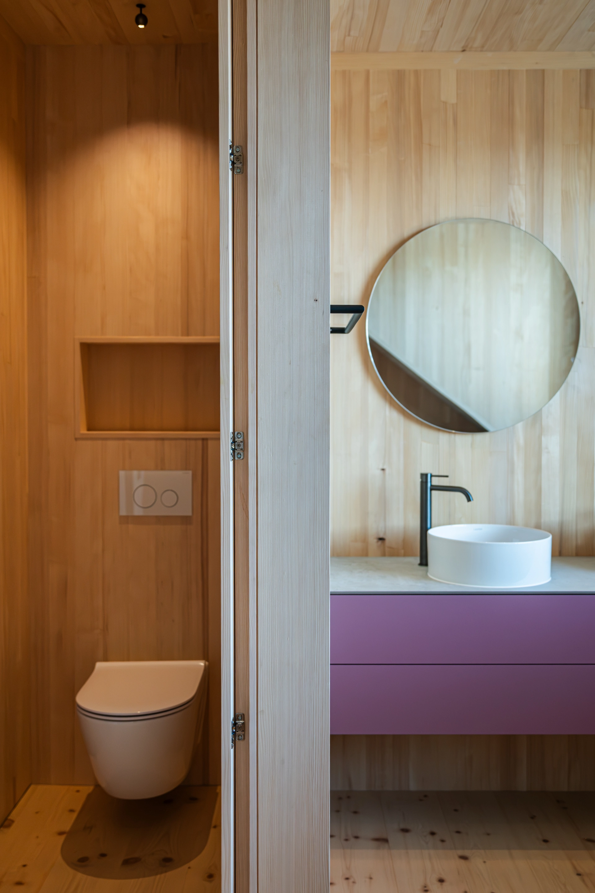Holzverkleidetes Badezimmer mit WC und farbigem Waschtischunterschrank