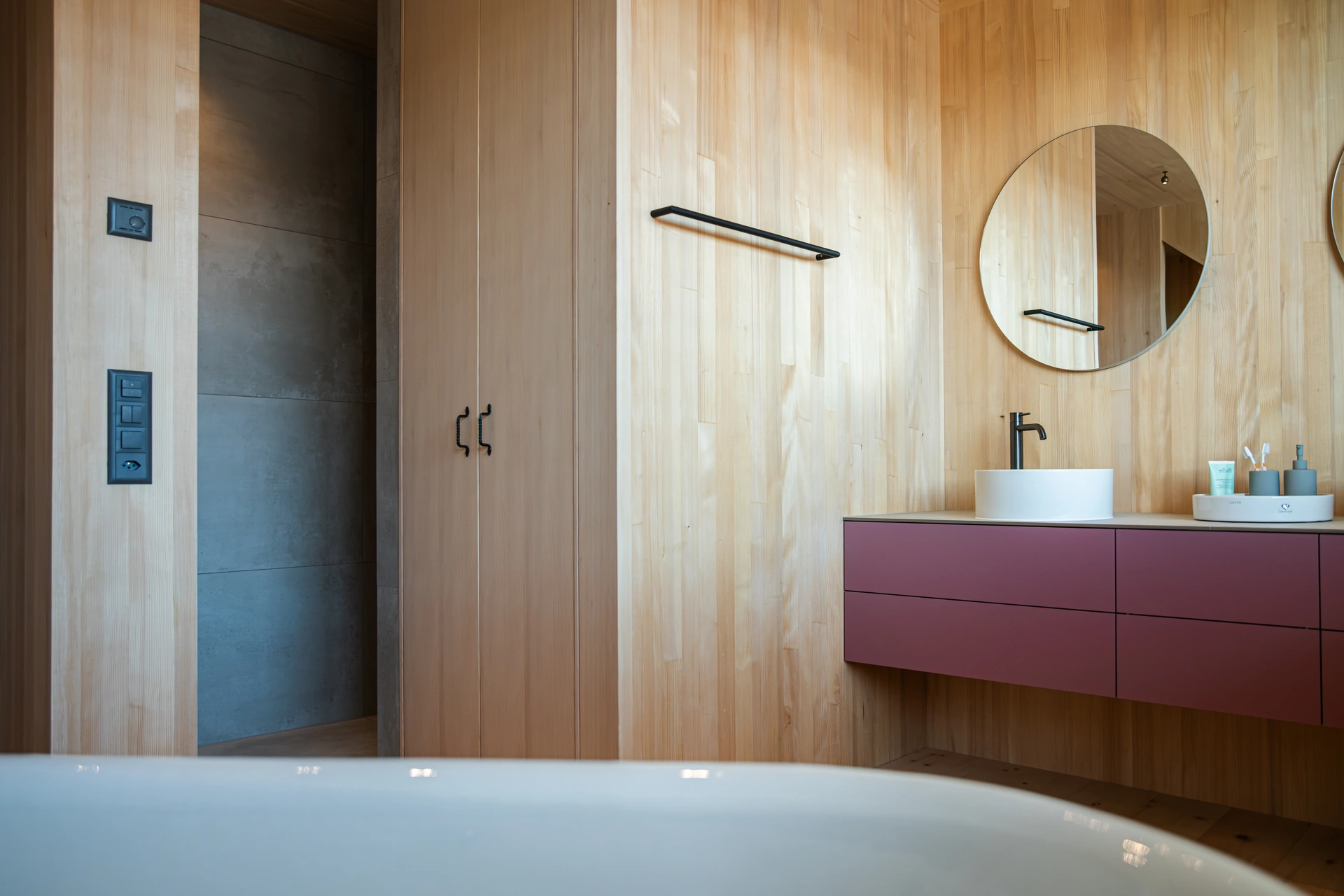 Holzverkleidetes Bad mit Waschplatz, runden Spiegeln und einer Badewanne im Vordergrund