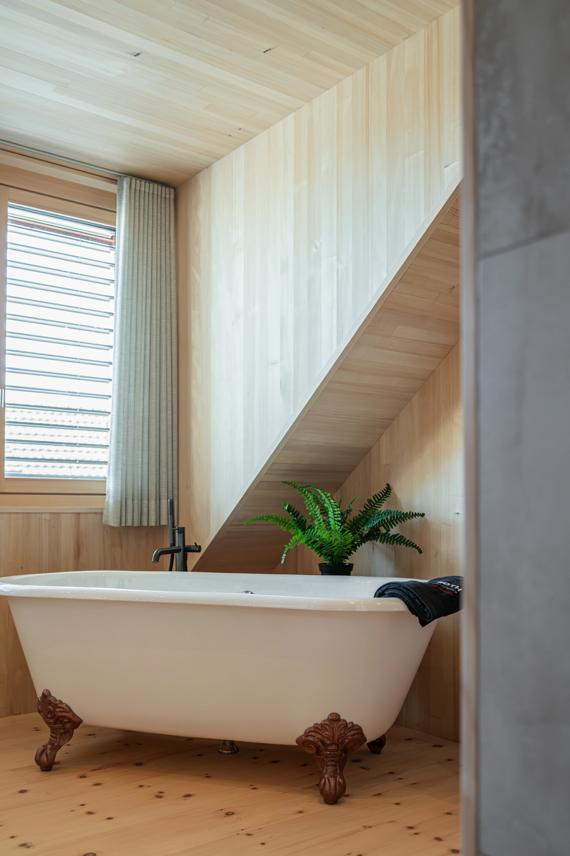 Freistehende weisse Badewanne auf verzierten Füssen in einem hellen Raum mit Holzverkleidung