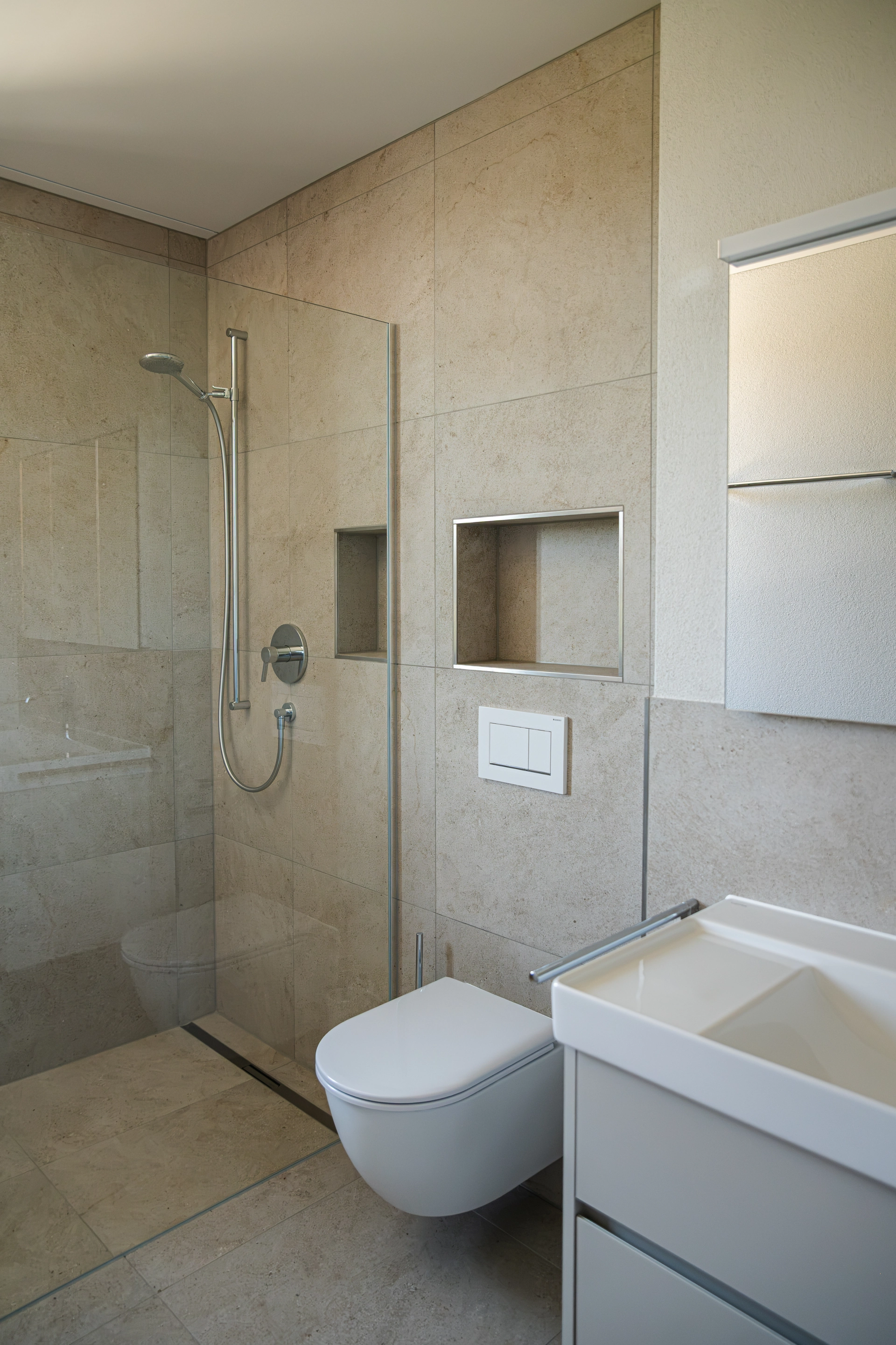 Badezimmer mit bodenebener Dusche, wandhängendem WC und weissem Waschtischunterschrank