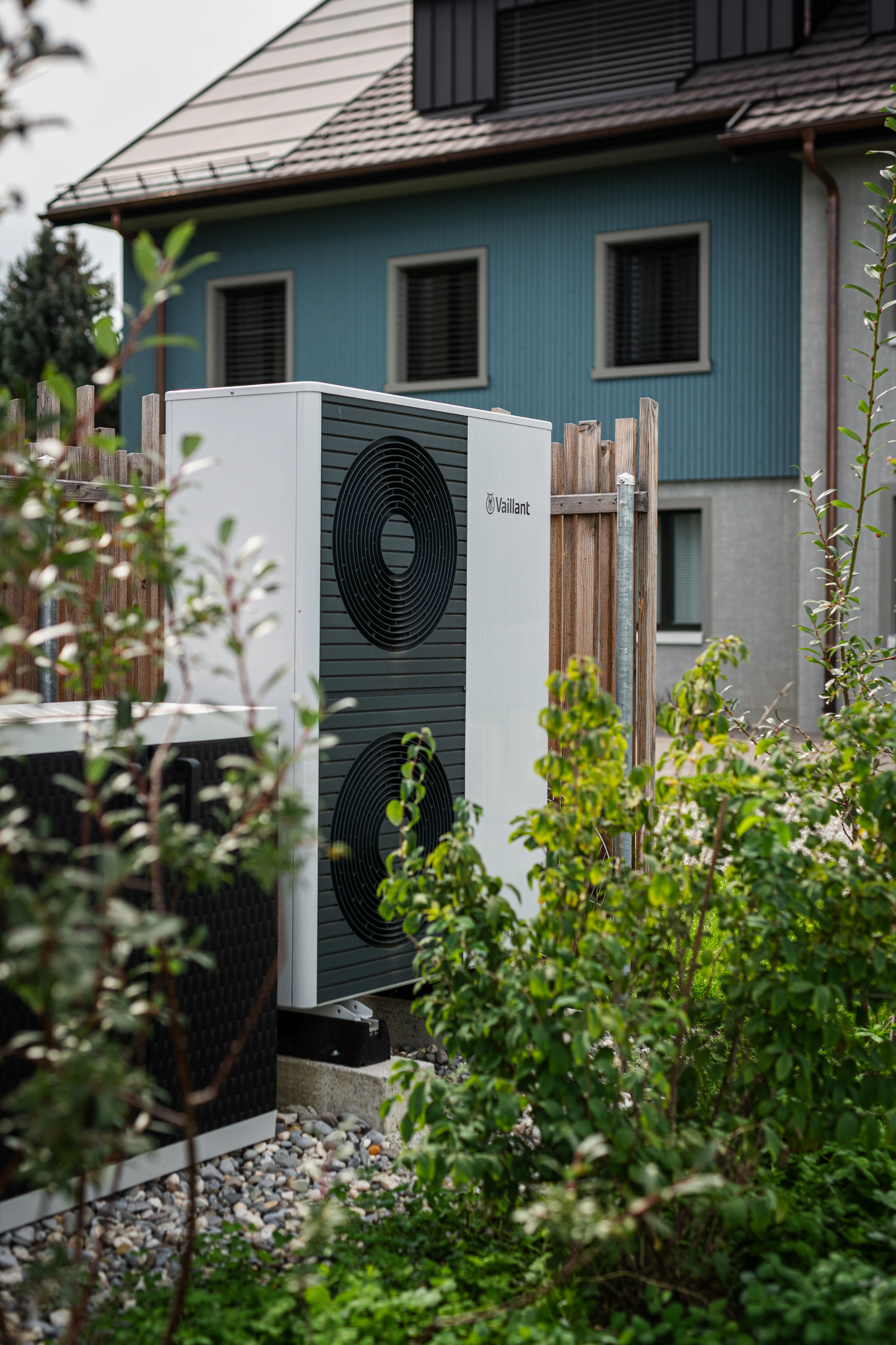 Ausseneinheit einer Wärmepumpe zwischen Gartenpflanzen vor einem Wohnhaus
